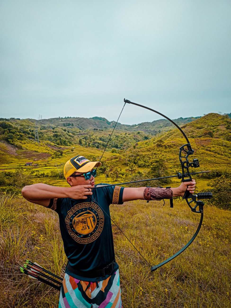 Archer at full draw outdoors, with the landscape behind