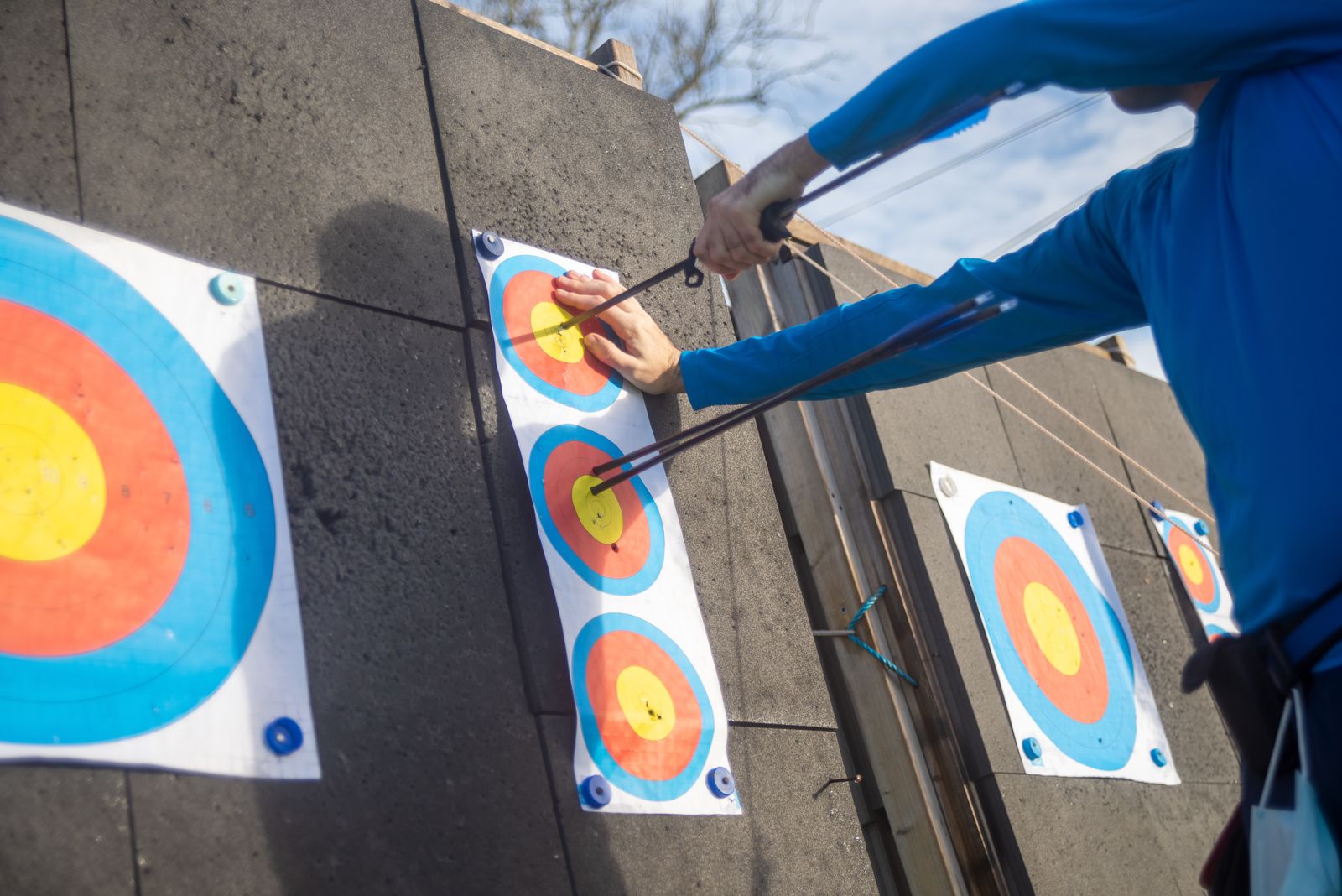Archer pulling arrows from a three-spot paper face on a target boss