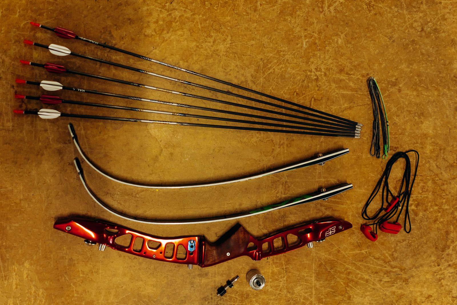 Arrows with fletching, limbs, riser and string of a recurve bow taken apart, seen from above on an amber background